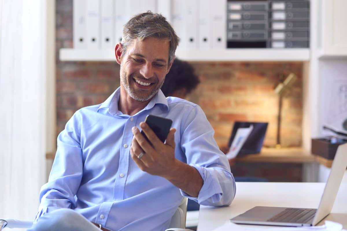 mature businessman working at desk in office messaging on mobile phone