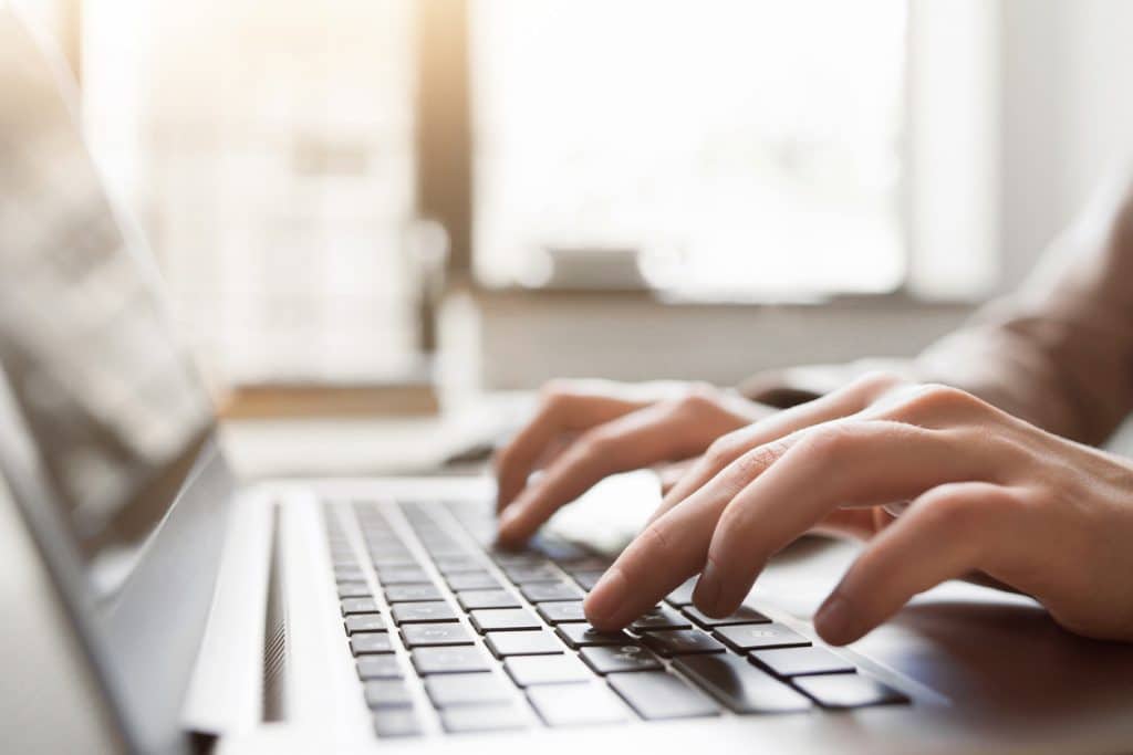 Close view of hands typing on a laptop keyboard in a bright room